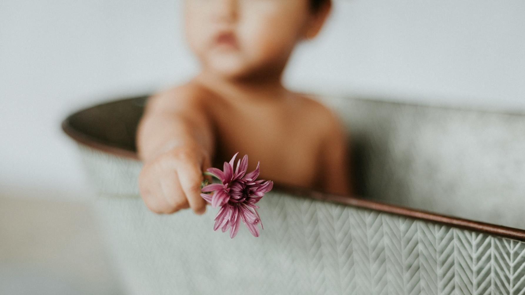 natural soap for babies close up shot of a baby sitting inside the bathtub while holding a blooming purple flower